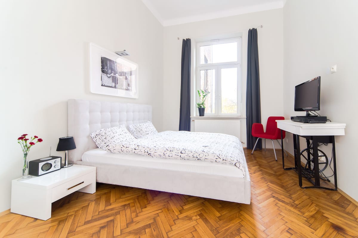 Un dormitorio con cama, mesita de noche, lámpara, radio y televisor sobre un escritorio.