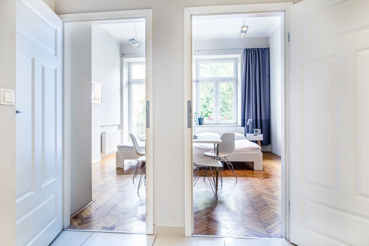 Un pasillo que conduce a un dormitorio con cama, mesita de noche y ventana con cortinas.