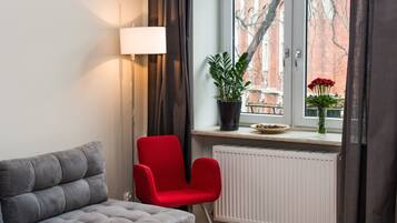 Un soggiorno moderno con un divano grigio, una poltrona rossa, una lampada da terra, una pianta in vaso e una finestra vista edifici.