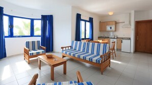 A modern living room with a sofa set, wooden chairs, a coffee table, and a kitchen area with a microwave and cabinets. - Apartamentos Club Pocillos (Tías)