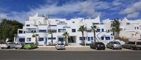 Un bâtiment blanc agrémenté de touches de bleu, doté de nombreux balcons et bordé de palmiers.