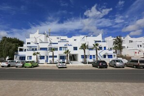A white building with blue accents, multiple balconies, and palm trees. - Apartamentos Club Pocillos (Tías)