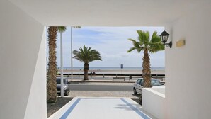 A view from a balcony overlooking a beach with palm trees, a paved walkway, and parked cars. - Apartamentos Club Pocillos (Tías)