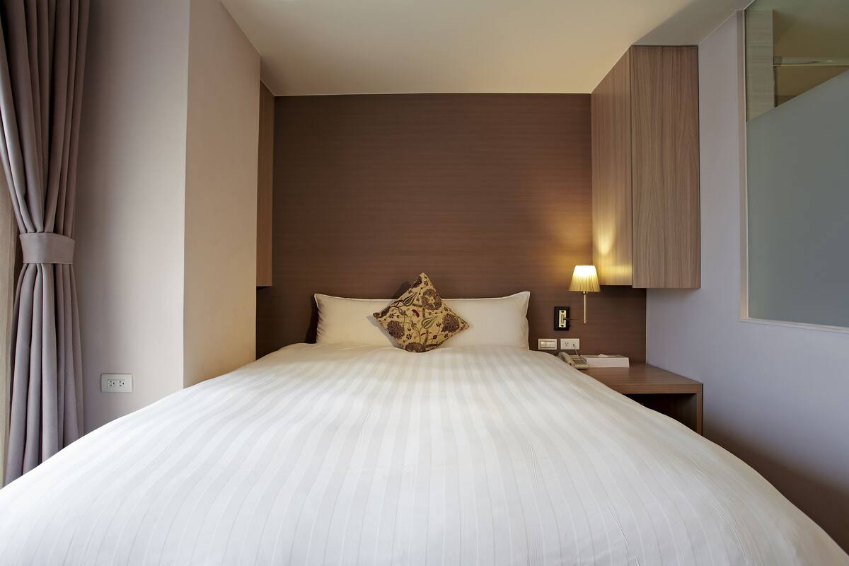 A hotel room with a large bed, a nightstand with a lamp, and a wooden headboard.