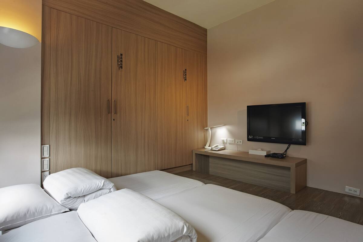 A hotel room with two beds, a TV, a bedside table with a lamp, and a wooden wardrobe.
