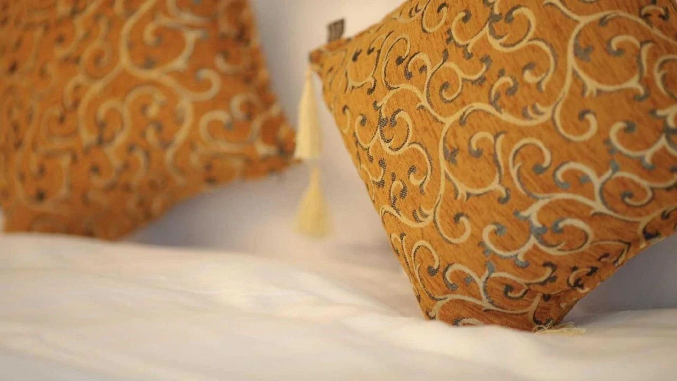 Een bed met een wit laken en twee sierkussens met een paisleimotief.