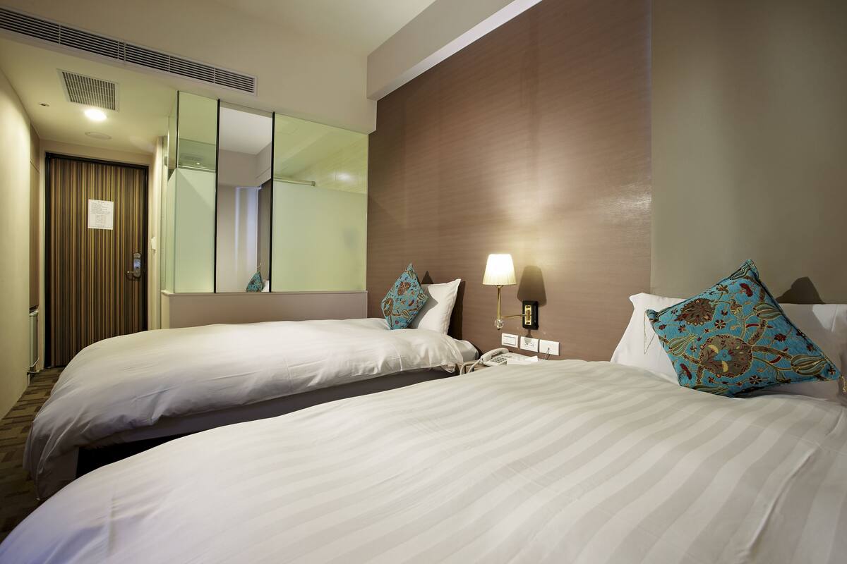 A hotel room with two beds, a large mirror, and a nightstand with a lamp.