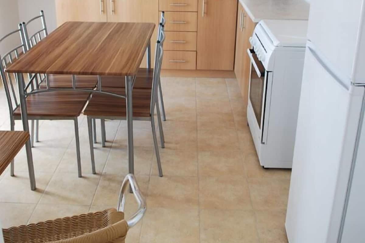 A compact kitchen with wooden cabinets, a white countertop, a stainless steel sink, a white refrigerator, and a dining table with metal chairs.