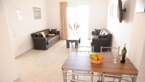 Una sala de estar moderna con un sofá, una mesa de comedor con sillas y un televisor montado en la pared.