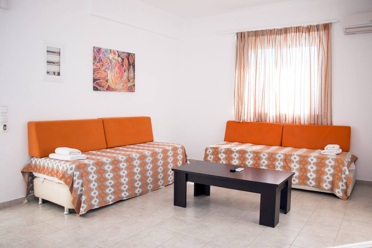A room with two orange sofas, a small table, and a colorful painting on the wall.
