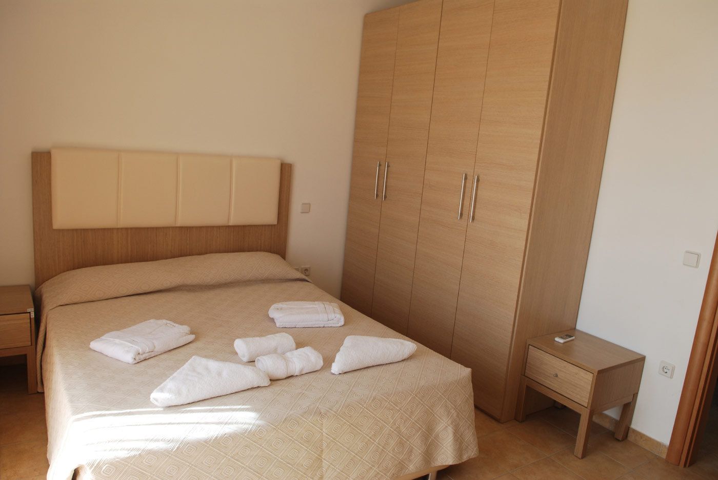 Un dormitorio con una cama grande, armario de madera, mesita de noche y velador.