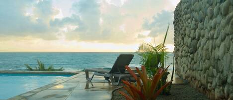 A pool area with a lounge chair, a pebble path, and a stone wall.