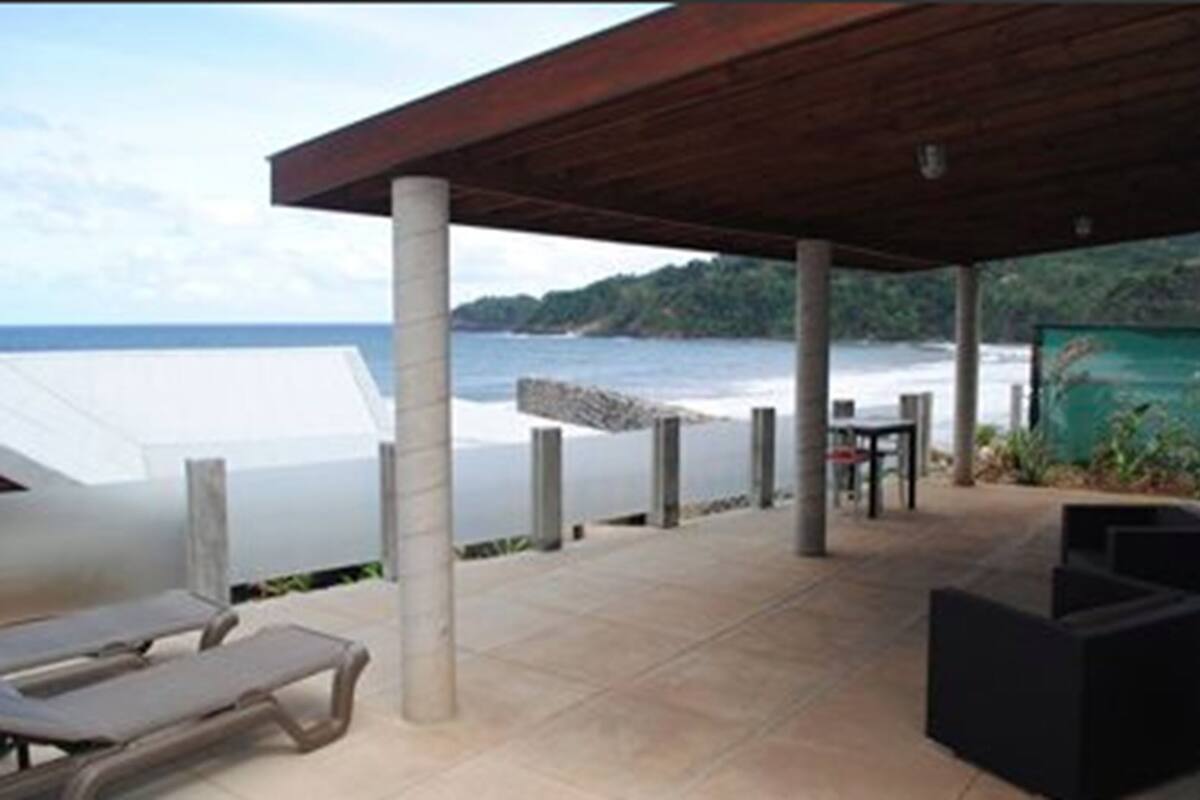 Un espace extérieur abrité, avec vue sur l’océan, comprenant un fauteuil de relaxation, une table et un barbecue.