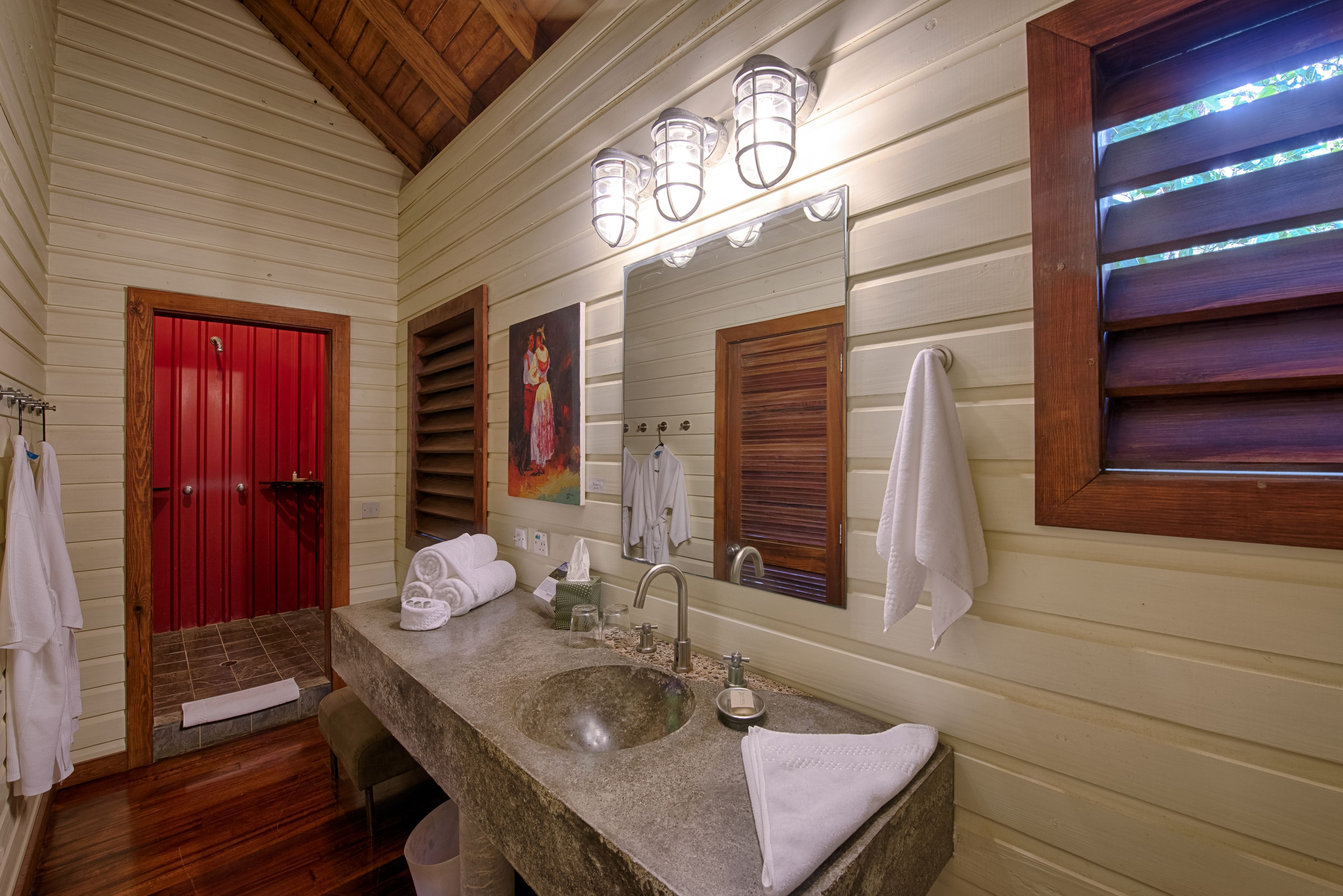 A bathroom with a large sink, a red door, and a mirror with lights.