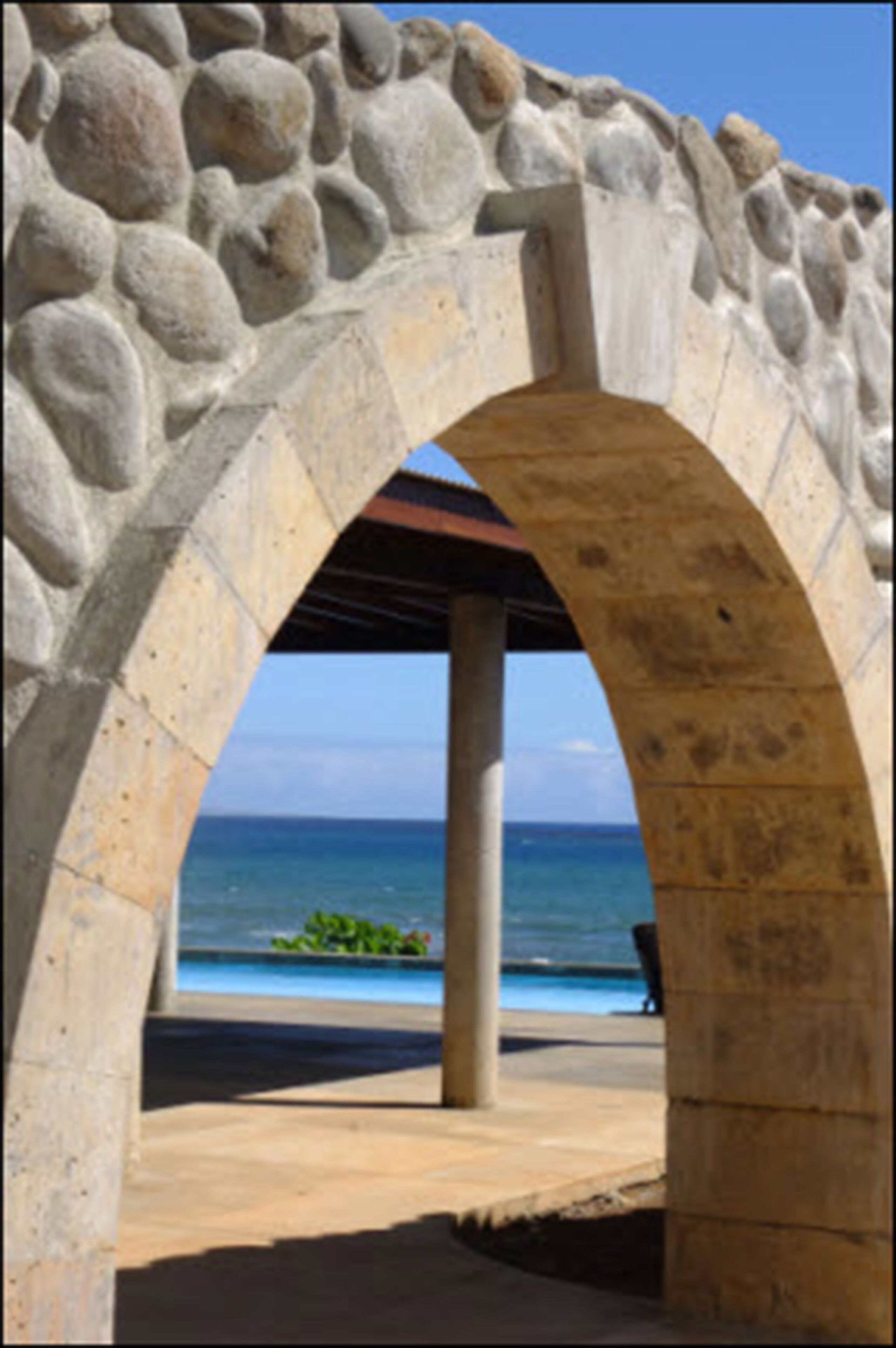 A stone archway leading to a beach with a clear view of the ocean.