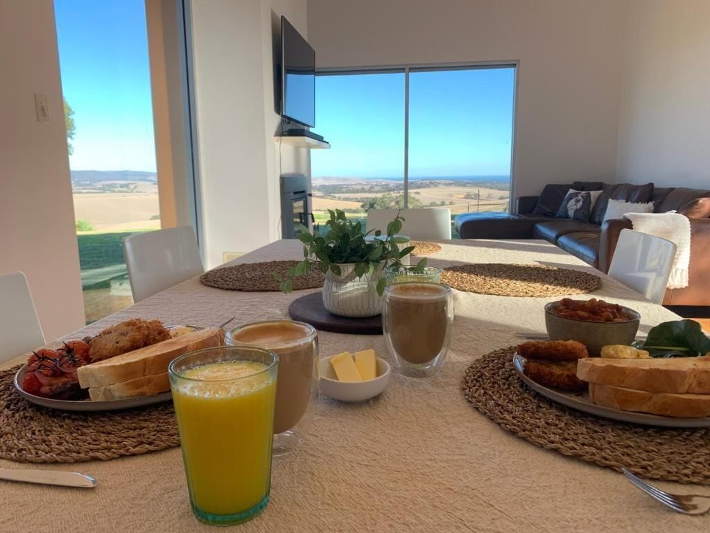 A breakfast table with a view of the countryside, a sofa, and a flat-screen TV in a modern room.