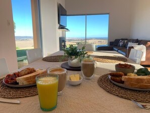 A breakfast table with a view of the countryside, a sofa, and a flat-screen TV in a modern room. - Lush Pastures (Bald Hills)