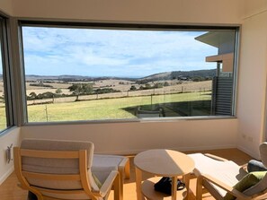 A room with a large window, a wooden chair, a small table, and a sofa. - Lush Pastures (Bald Hills)
