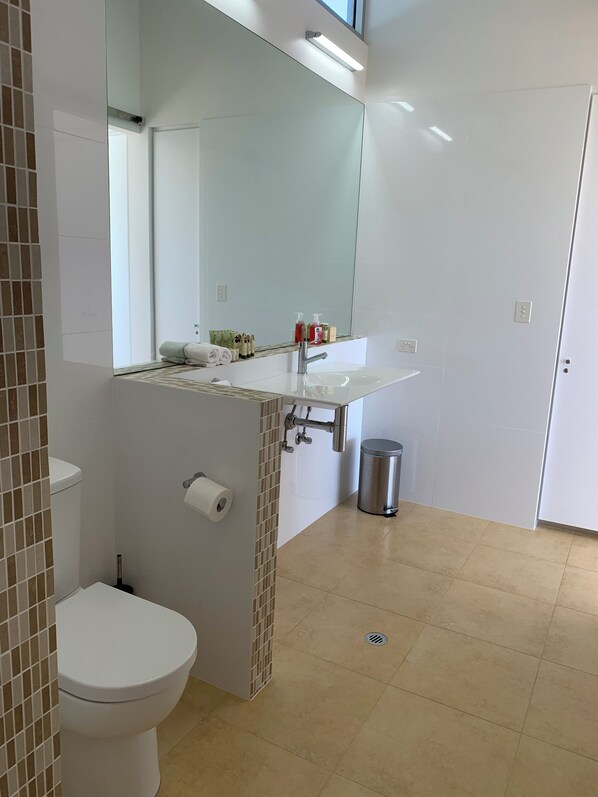 Un baño con inodoro blanco, un lavabo con espejo arriba y un cubo de basura.