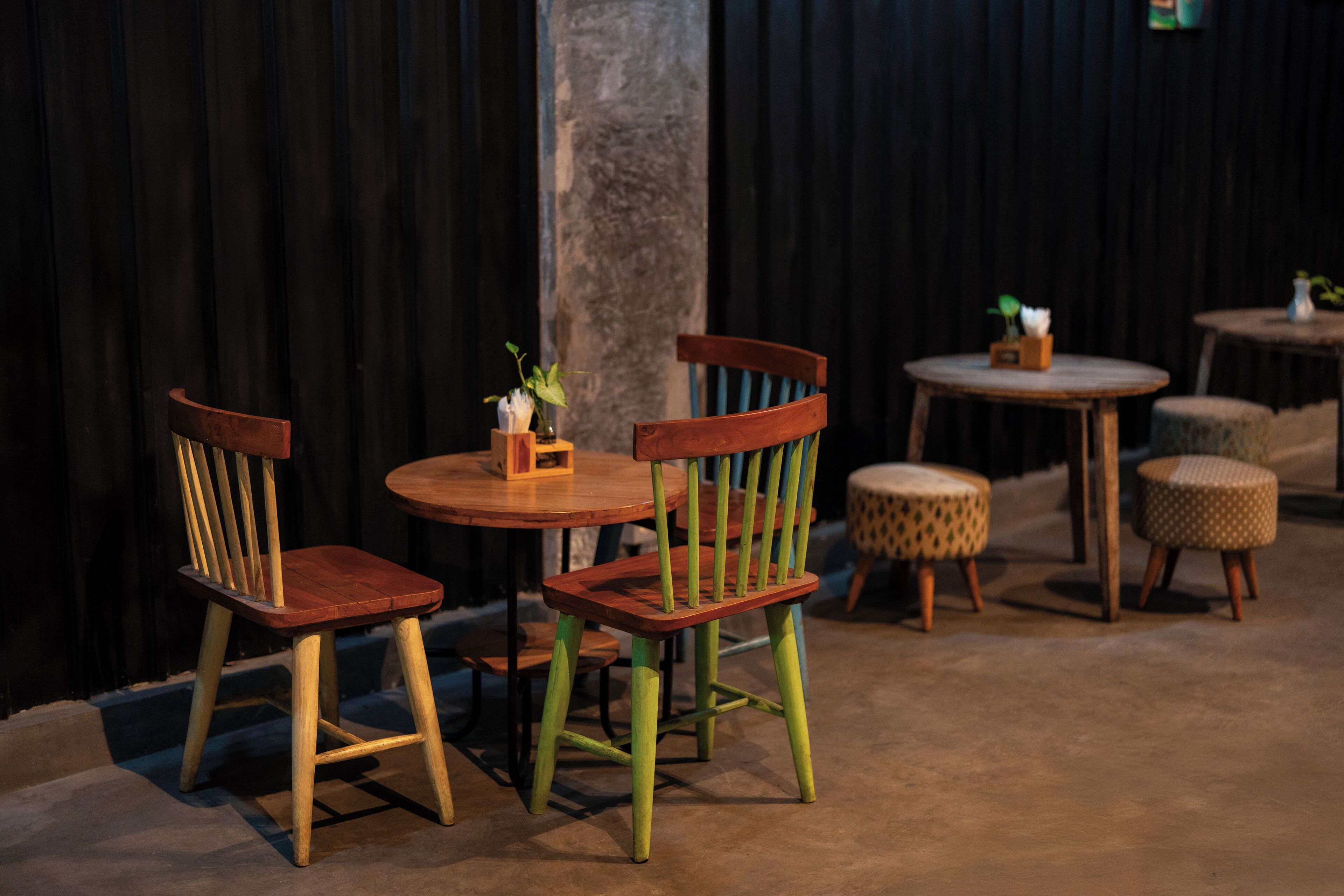 A dining area with wooden chairs and tables, a concrete pillar, and a dark curtain backdrop.