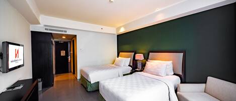 A hotel room with two beds, a sofa, a TV, and a desk.