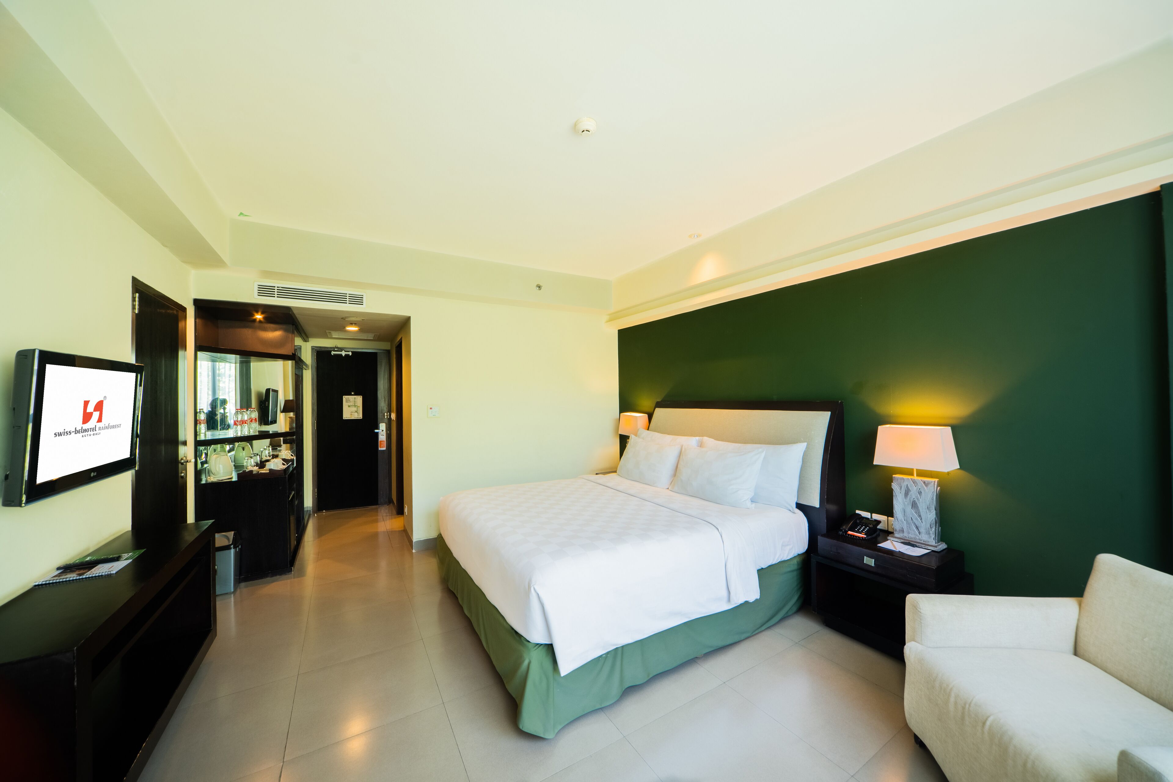 A hotel room with a bed, bedside table, lamp, and a TV on the wall.