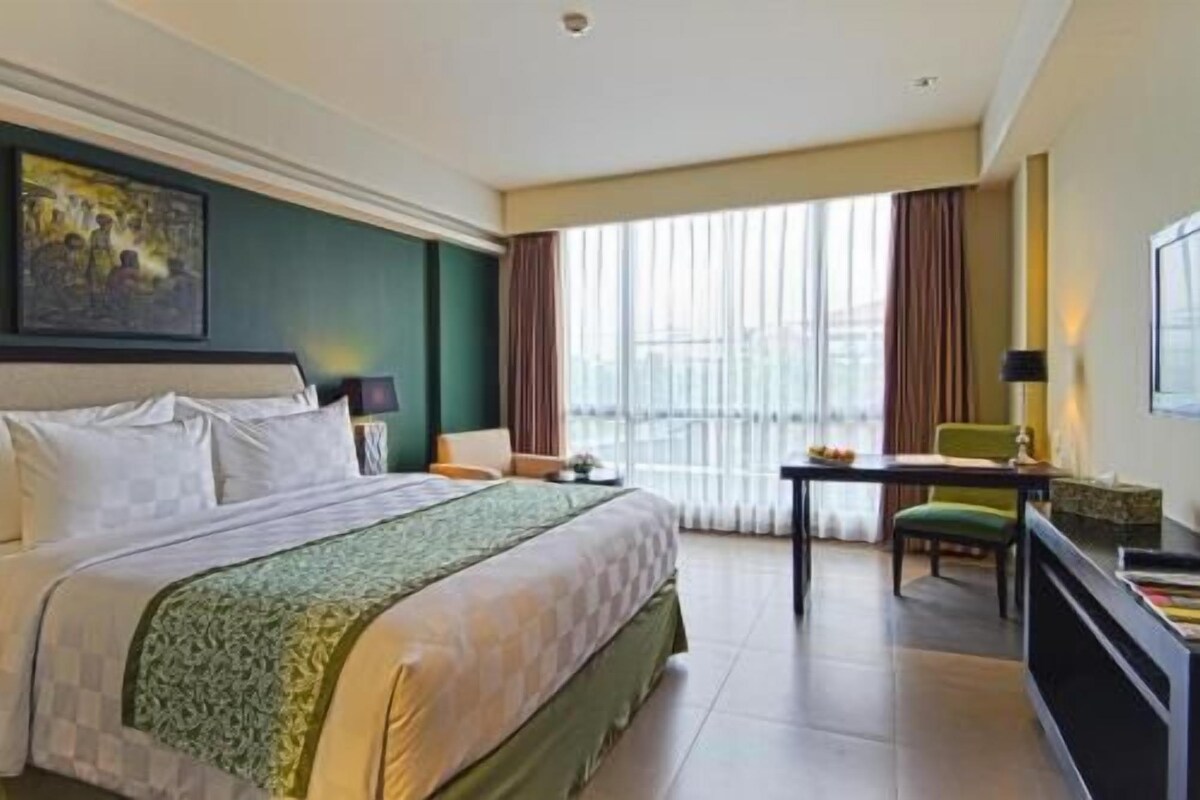 A hotel room with a bed, a desk, a chair, a television, and a window with curtains.