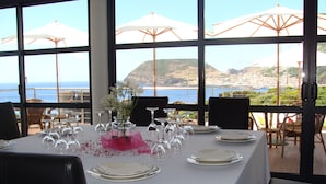 Une table dressée pour le dîner, avec vue sur la mer et les collines.