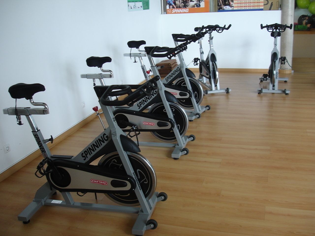 A row of stationary bikes in a room with wooden flooring and white walls.