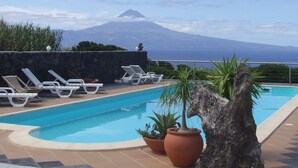 Un espace piscine avec des chaises longues, un grand tronc d’arbre et une vue sur une montagne.