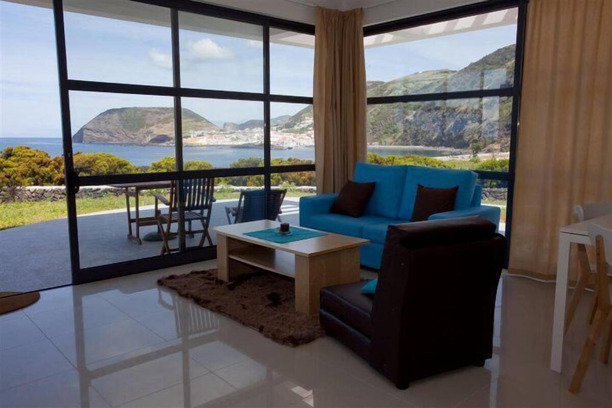 Un salón moderno con un gran ventanal que da a un balcón y vistas panorámicas del océano.