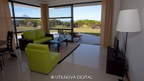 Un salon moderne avec un canapé, une table basse et des fauteuils, de grandes fenêtres offrant une vue sur un paysage montagneux.