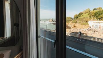 A view from a window overlooking a beach with people, a road, and a building with arches.