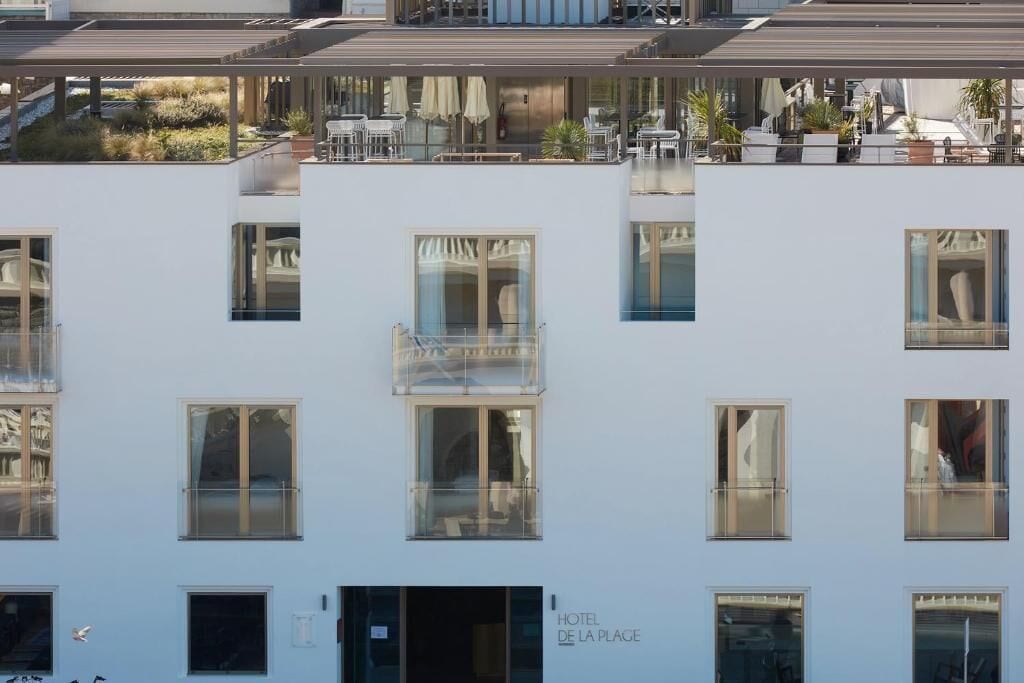 A multi-story hotel with balconies, large windows, and a sign reading "HOTEL DE LA PLAGE".