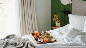 A neatly made bed with a tray of breakfast items, a green wall, and a window with curtains.