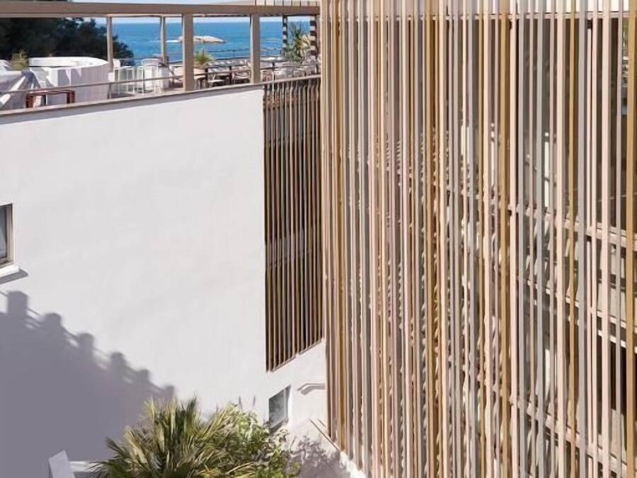 A modern building with a vertical wooden facade and a rooftop terrace with lounge chairs and umbrellas.