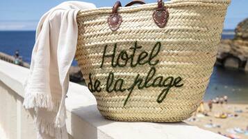 Un sac de plage en tissu tressé, doté de poignées et sur lequel est drapée une serviette, est posé sur une rambarde au bord de la mer.
