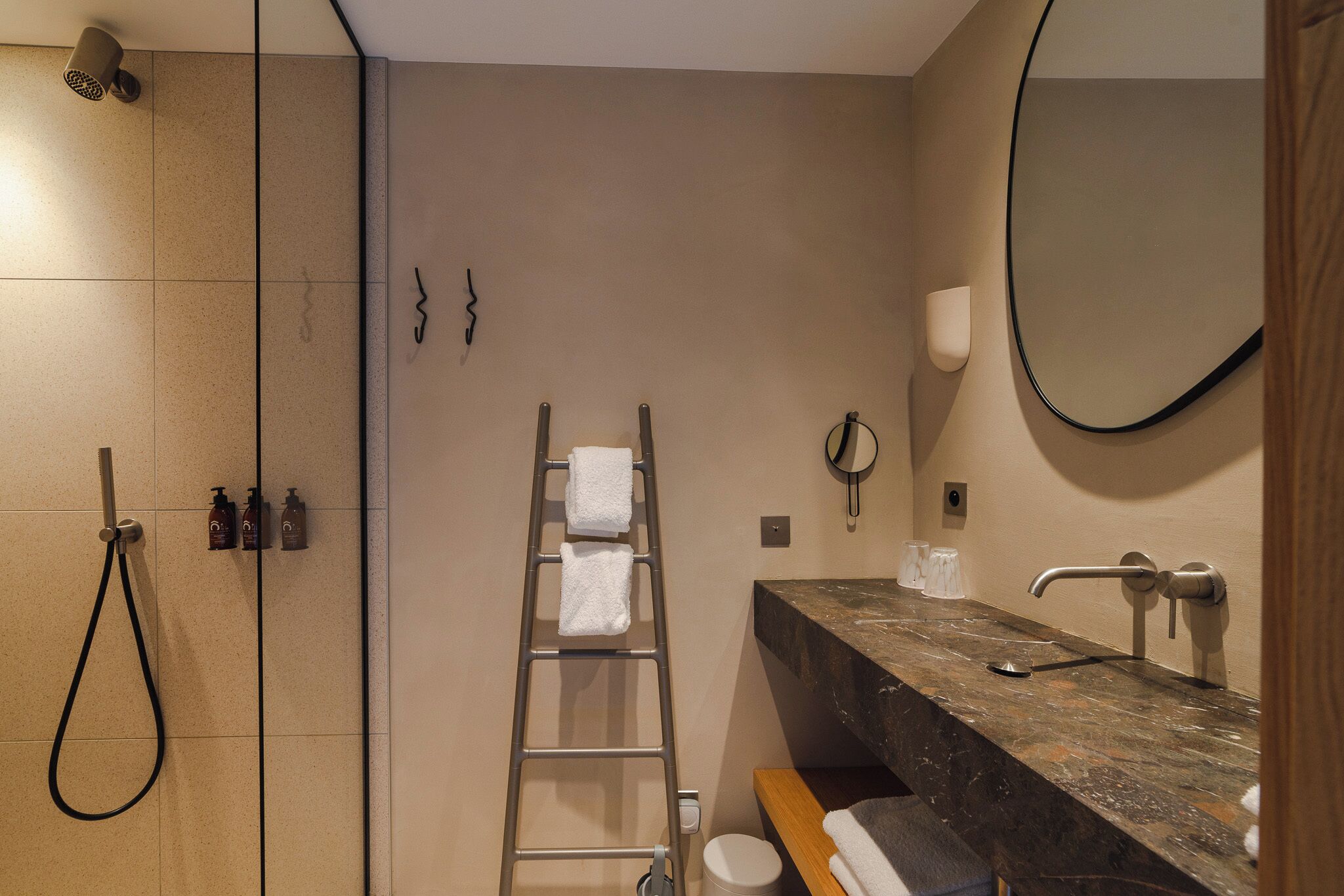 Un bagno moderno con cabina doccia in vetro, una panca in legno, un lavabo in marmo e uno specchio grande.
