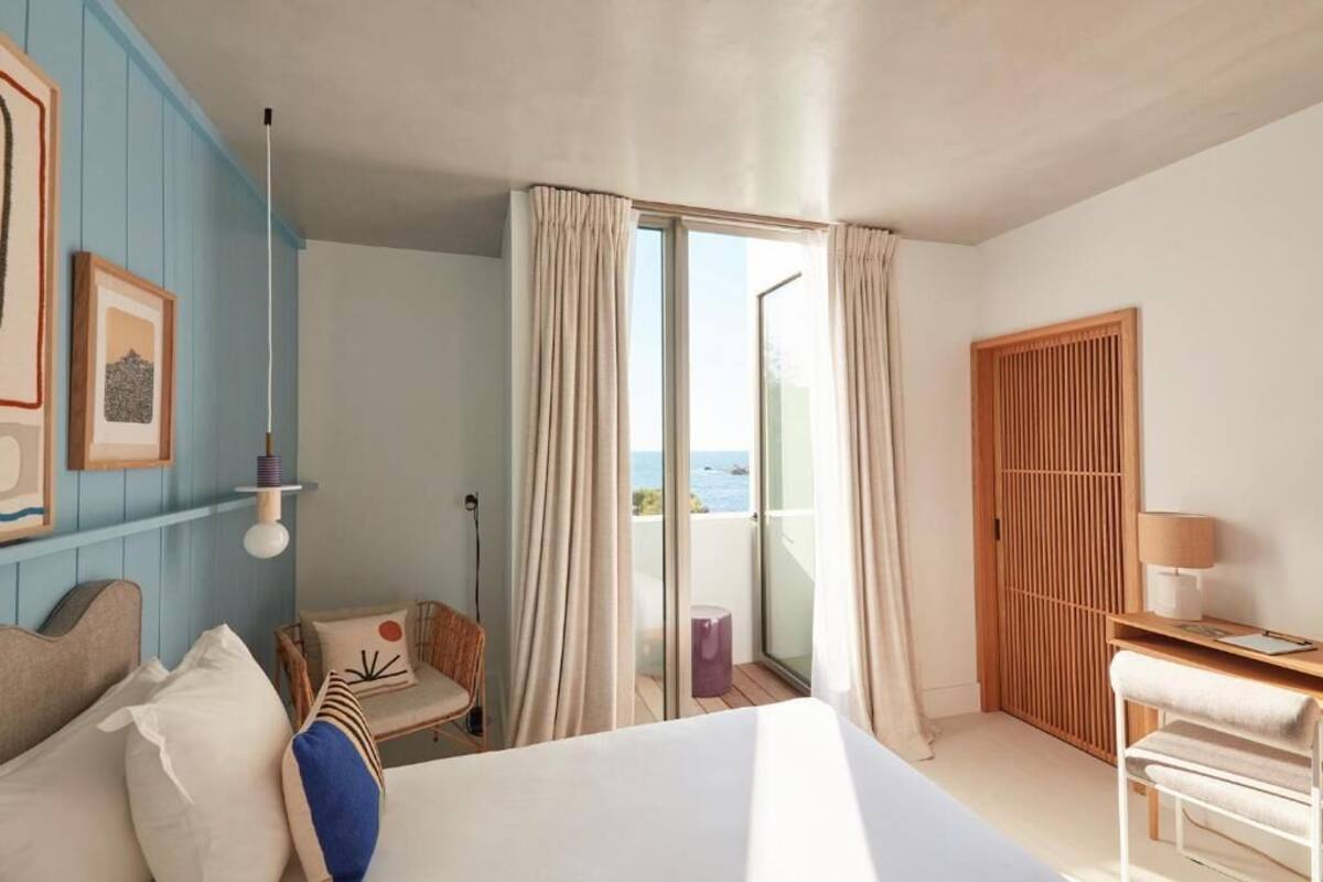 Ein Hotelzimmer mit Bett, Schreibtisch, Stuhl und Meerblick durch eine Schiebetür.