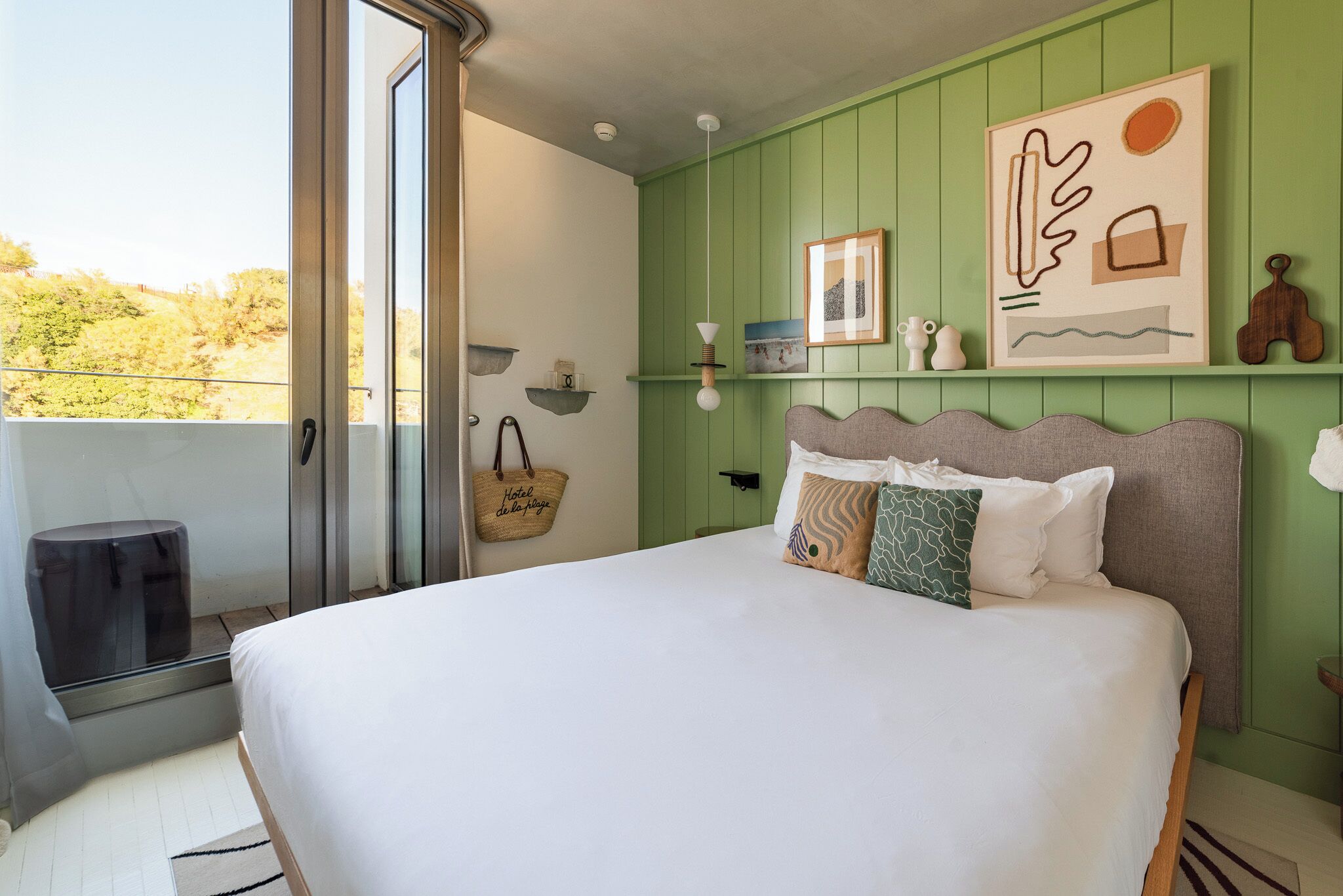 A bedroom with a bed, a green wall, a window, and a hanging light fixture.