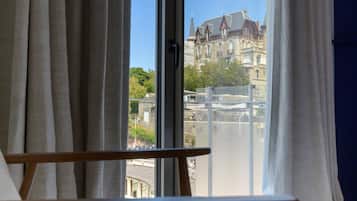 A room with a view of a building through a window with curtains.