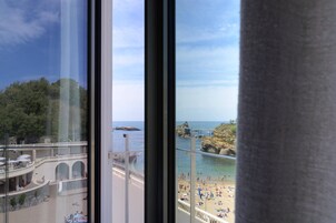 Vista desde una habitación de hotel con vistas a una playa, un promontorio rocoso y un muelle.