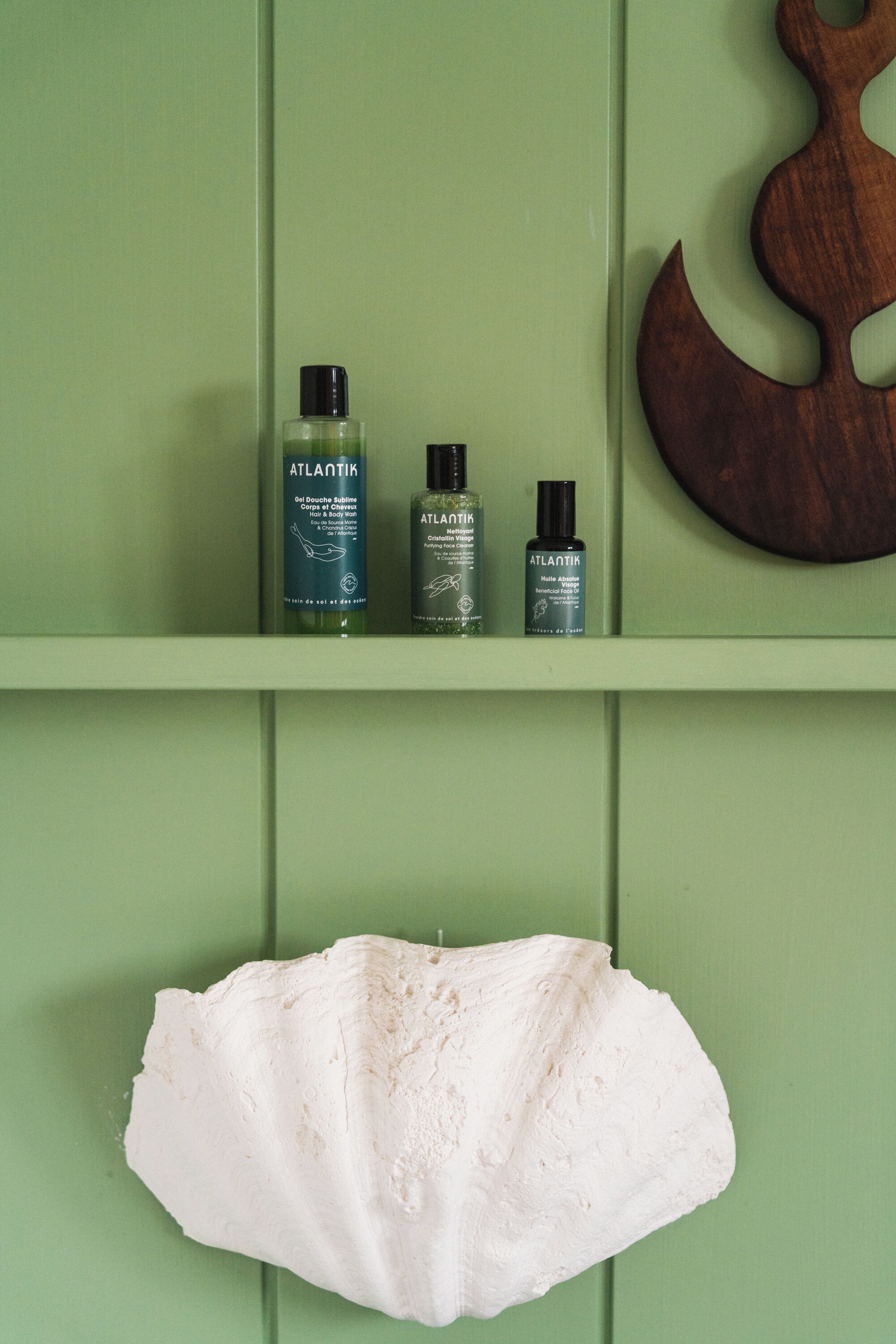 Une étagère avec trois bouteilles de produits de soins pour la peau de la marque Atlantic, et un grand objet blanc suspendu en dessous.