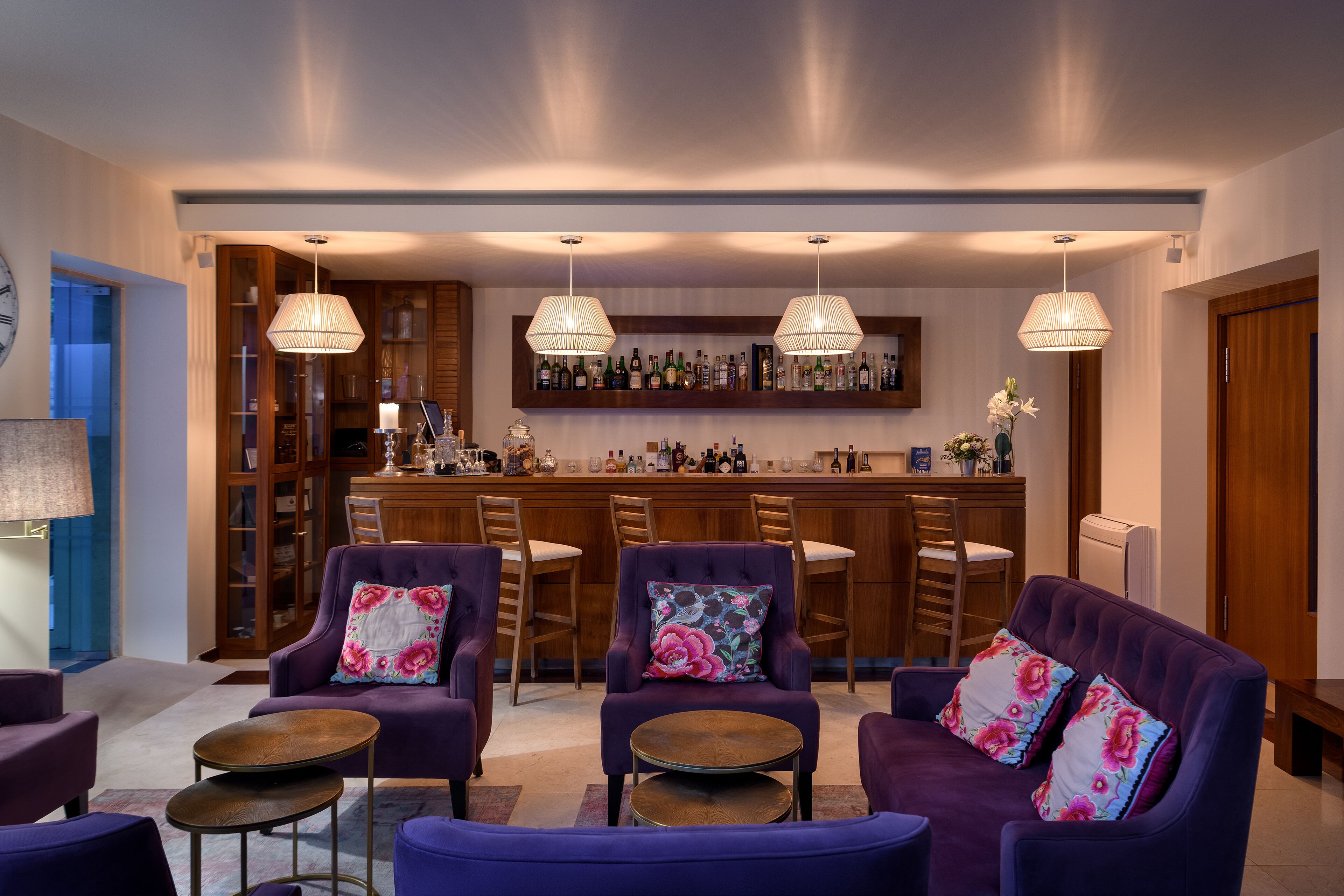 Una sala de estar moderna con un área de bar, que incluye sillones morados, una mesa de centro redonda y una estantería de madera.