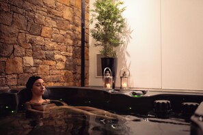 Um espaço de spa com parede de pedra, planta em vaso e banheira de hidromassagem.