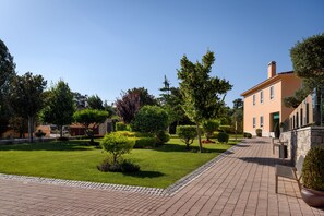 A courtyard with a paved walkway, neatly trimmed hedges, and a building with a stone facade.