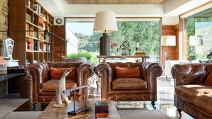 A spacious living room with leather sofas, a coffee table, and a bookshelf filled with books. - Hotel de Charme Casa da Amieira (Santarém)
