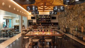 A spacious dining area with multiple tables and chairs, a stone wall, and modern lighting fixtures.
