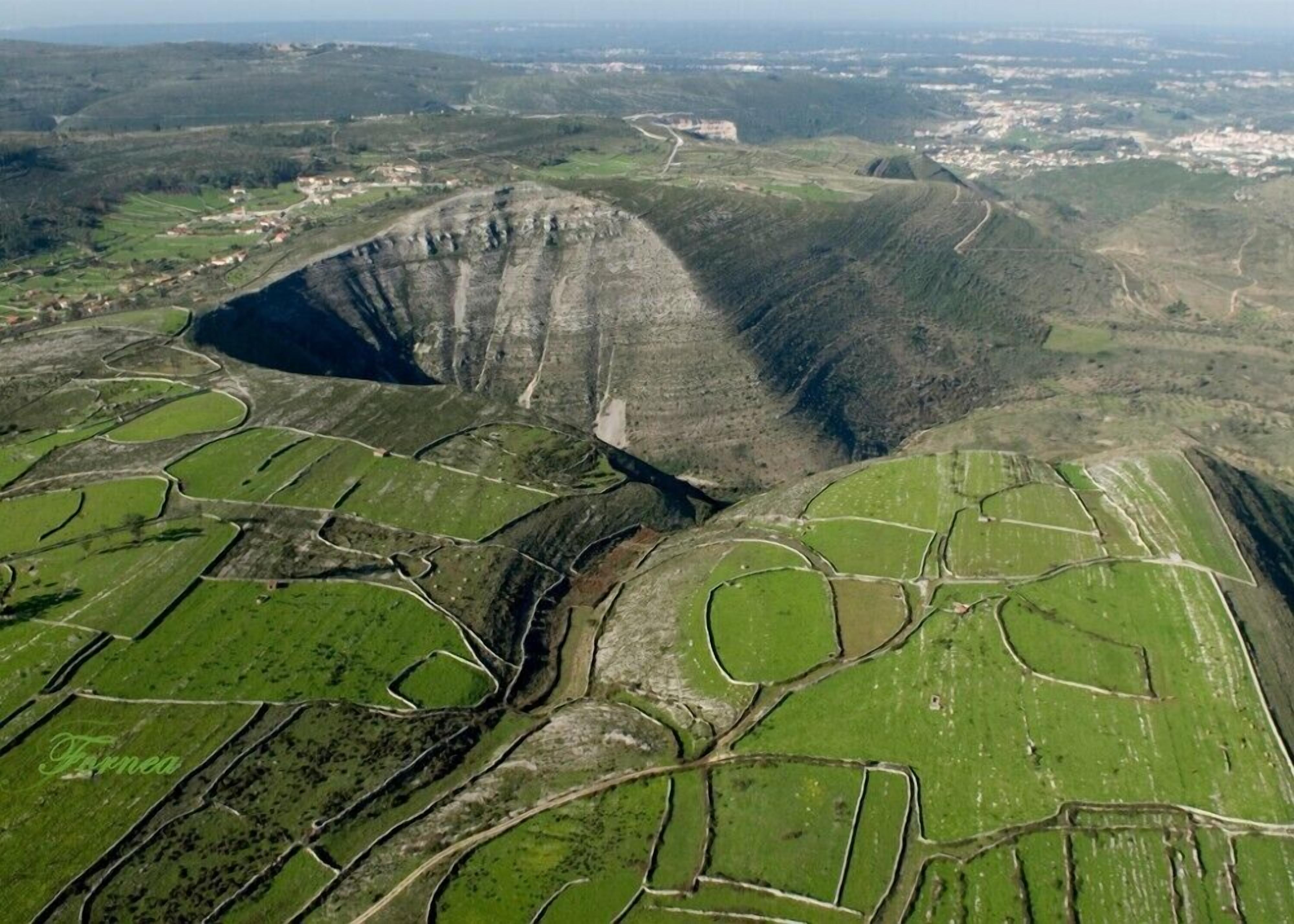 Luchtbeeld van een vallei met terrassen en velden en een grote, steile depressie.