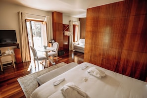 Habitación de hotel con una cama grande, un escritorio con televisor, una silla y una pequeña mesa con una taza y un platillo.